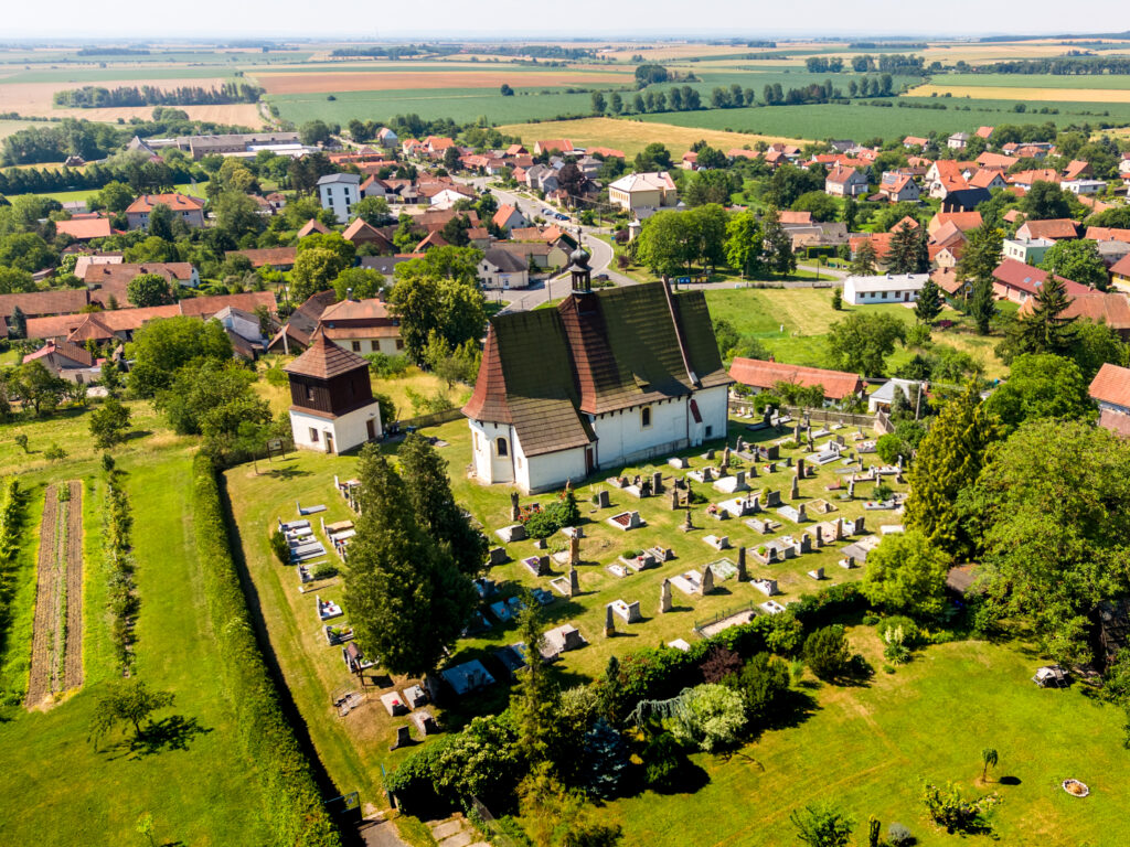 Letecký pohled na obec Mcely s kostelem, zelení a okolní krajinou ve Středočeském kraji